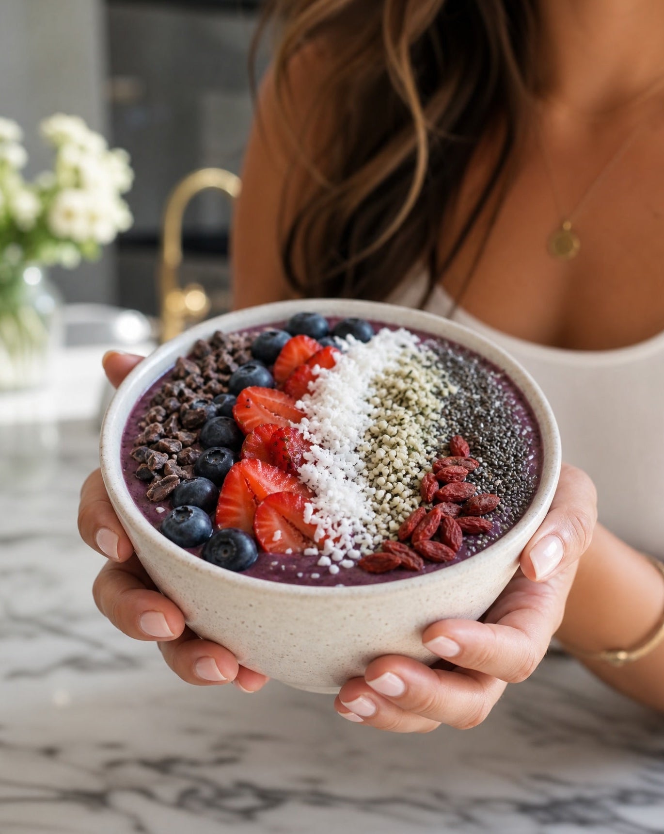 Person holding a bowl of acai bowl with toppings in a kitchen setting